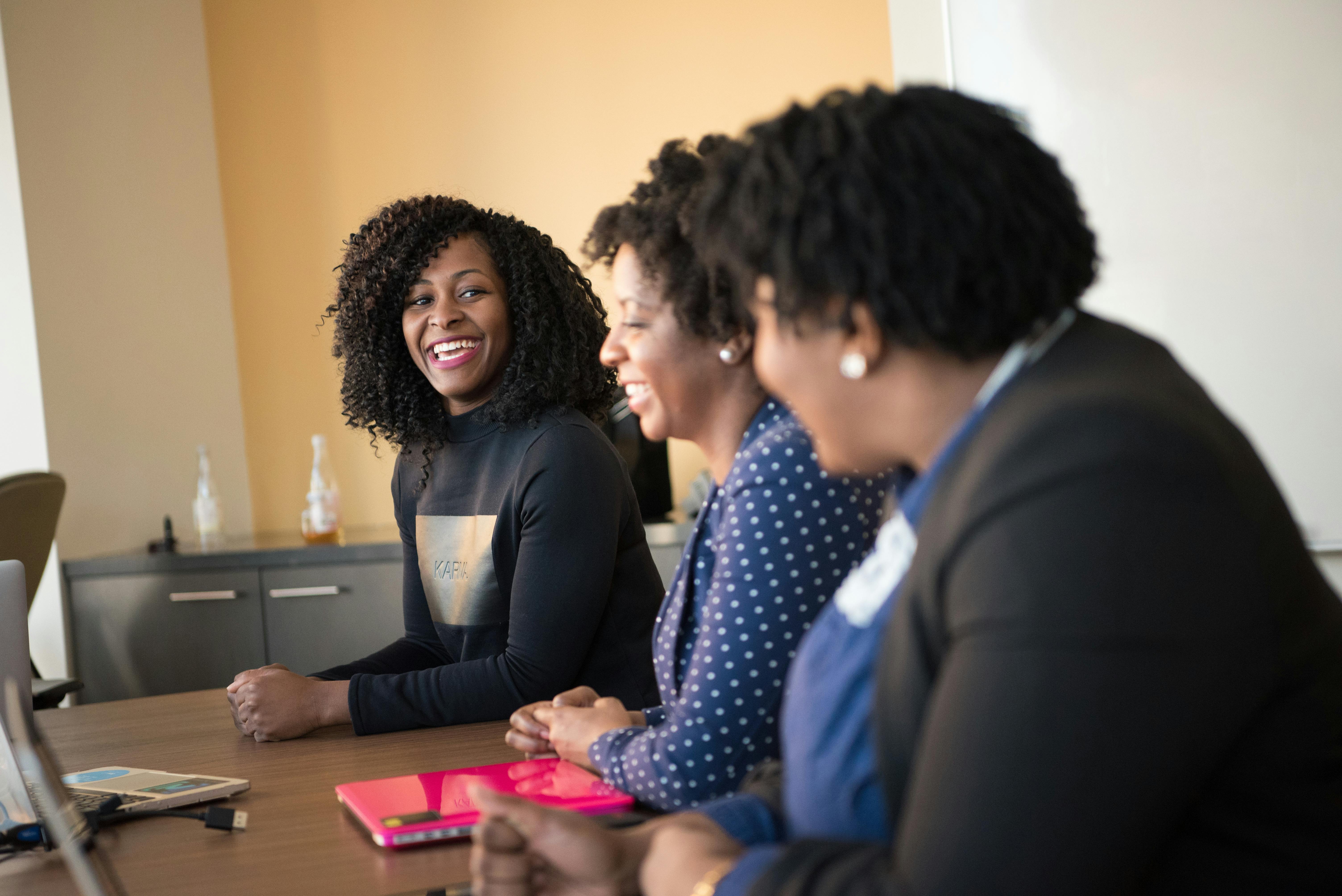 Three black women in a happy office meeting, engaging in teamwork.