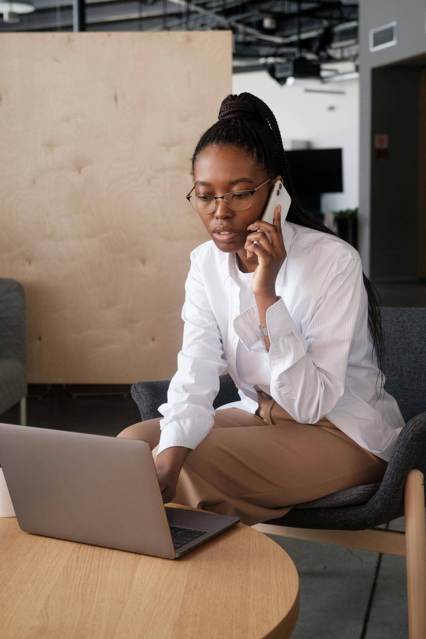 African American businesswoman talking on smartphone while working on laptop indoors.